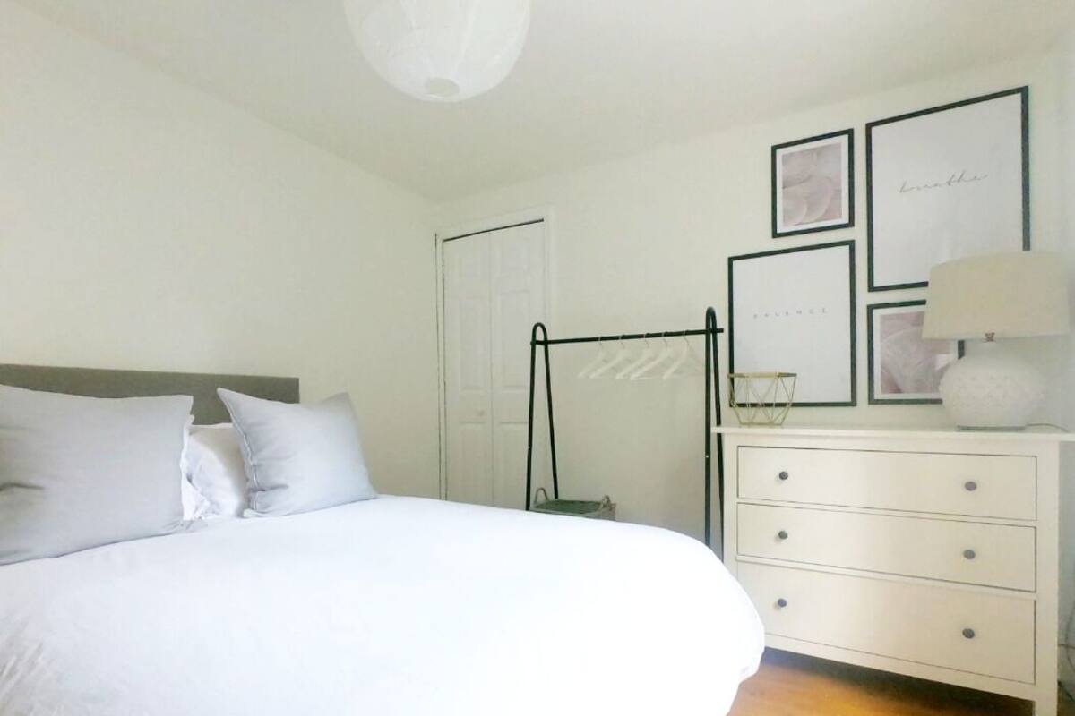 A bedroom with a bed, a dresser, a lamp, and framed pictures on the wall.