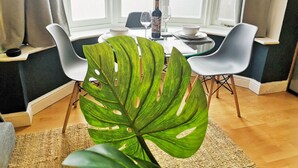 Zona pranzo con tavolo in vetro, sedie bianche e una pianta verde grande in primo piano.