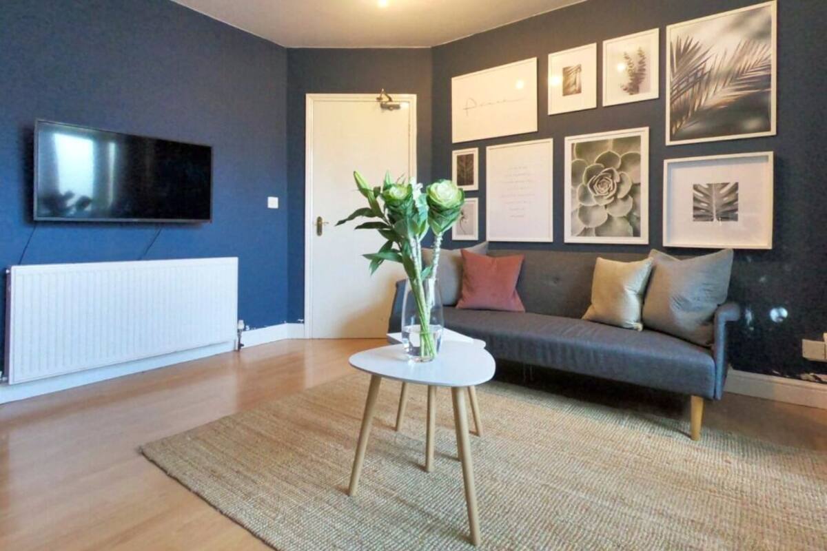 A modern living room with a grey sofa, a white coffee table with a vase of green plants, and framed artwork on the wall.