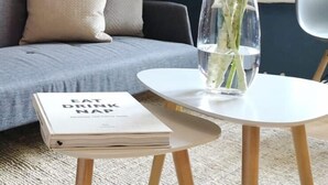 Un soggiorno con un divano grigio, un tavolino bianco e un vaso con piante verdi.