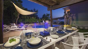 An outdoor dining area with a pool, white chairs, and a table set for a meal. - Villa Felice (Massa Lubrense)