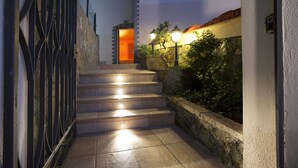 A staircase leading to a door with a warm light source above it, surrounded by stone walls and a metal gate. - Villa Felice (Massa Lubrense)