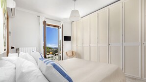 A bedroom with a large bed, white walls, a wardrobe, a TV, and a view of the outdoors. - Villa Felice (Massa Lubrense)
