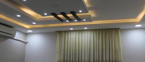 A room with a modern ceiling design featuring recessed lighting and a central air conditioning unit.