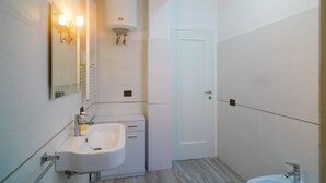 A bathroom with a white sink, mirror, and toilet. There is a white door and a light fixture above the sink. - Appartamento Molo B (Portoferraio)