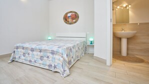 Un dormitorio con cama, mesita de noche, espejo y baño con lavamanos.