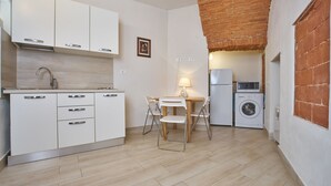 Una cocina compacta con armarios blancos, una mesa de comedor de madera y una lavadora.