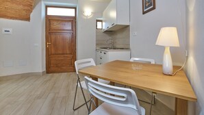 Un comedor con una mesa de madera, sillas blancas, una lámpara y una cocina al fondo.