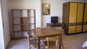 Une pièce avec une table et des chaises en bois, un téléviseur posé sur une petite table, une bibliothèque et une armoire à portes coulissantes.