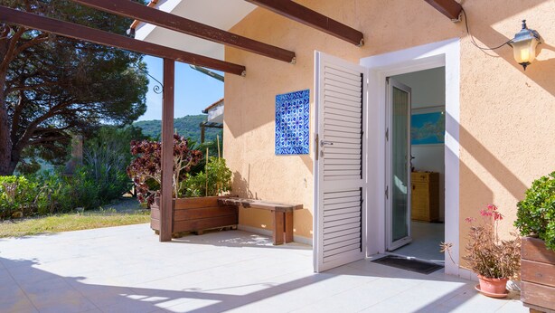 A covered patio with a wooden bench, a potted plant, and a door leading to an interior space. - Appartamento Poggio Al Sole (Capoliveri)