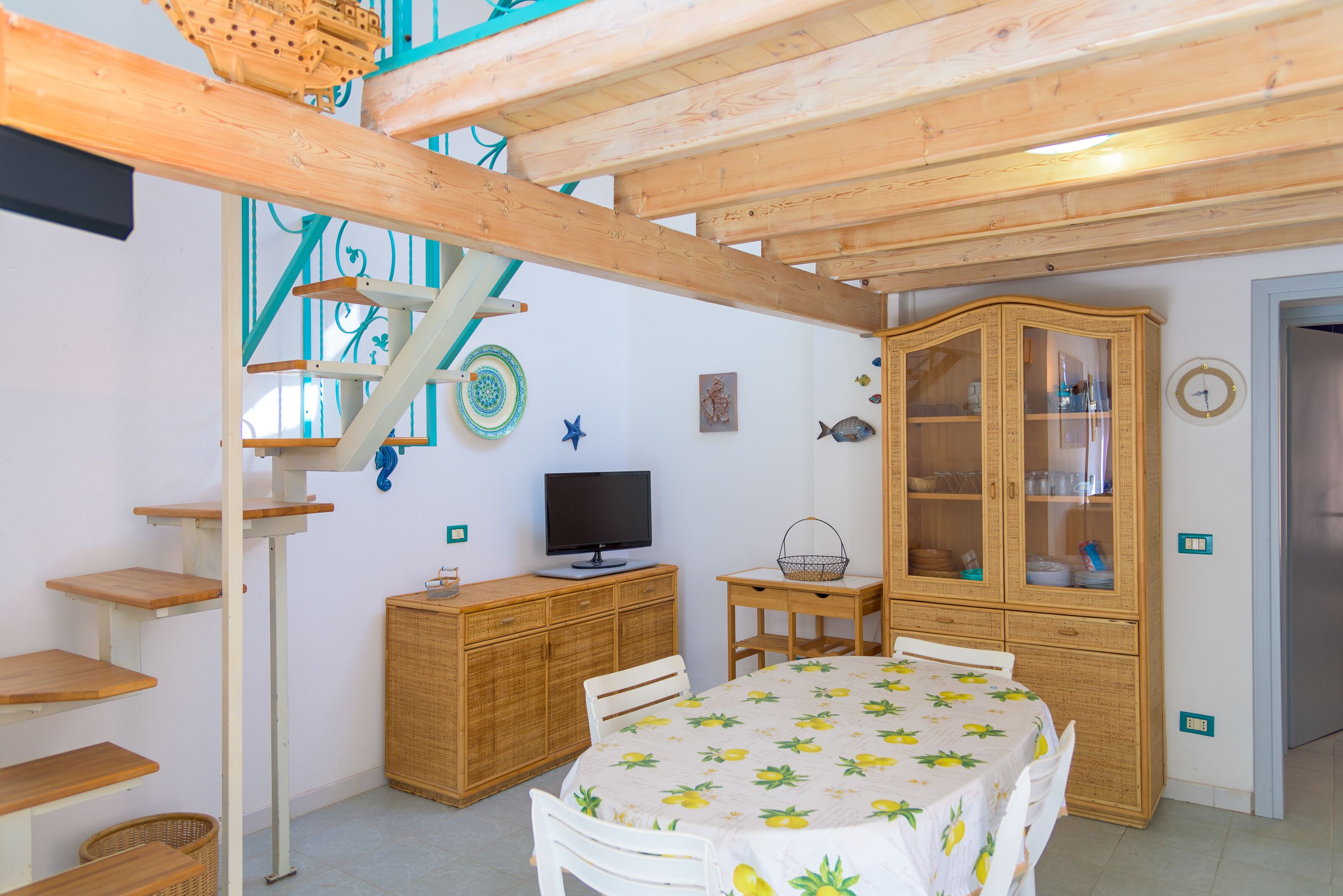 Una habitación con techo de madera, una mesa de comedor con mantel, un televisor sobre un mueble de madera, un adorno de pez en la pared y un aparador con puertas de cristal.