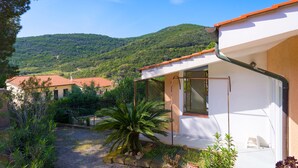 A house with a red-tiled roof, a white exterior, and a garden with a palm tree. - Appartamento Poggio Al Sole (Capoliveri)