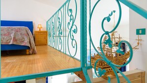 A bedroom with a bed, a wooden nightstand, a lamp, and a decorative ship model. - Appartamento Poggio Al Sole (Capoliveri)