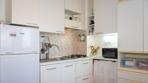 A kitchen with white cabinets, a white refrigerator, a gas stove, and a sink. - Appartamento Porto Mediceo (Portoferraio)