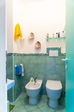A bathroom with two toilets, a bidet, and a sink. There are towels hanging on the wall and toiletries on a shelf. - Appartamento Porto Mediceo (Portoferraio)