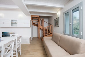 A modern interior with a wooden staircase, a beige sofa, and a dining area with white chairs and a table.