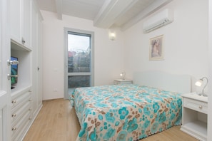 A bedroom with a bed, a nightstand, a desk, a wardrobe, and an air conditioning unit.