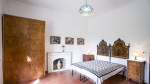 Ein Schlafzimmer mit Bett, Holzschrank, Kamin und Wandbild.