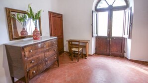 Ein Zimmer mit einem Holzkasten, einem Stuhl, einem Spiegel und einer Tür mit einem Rundbogenfenster.