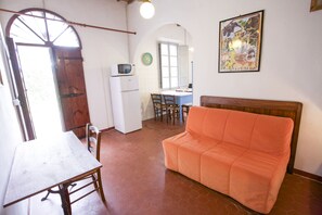 Una stanza con un tavolo in legno, un divano, un angolo cottura con frigorifero e forno a microonde, e una finestra vista esterna.