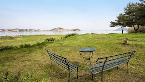 Een gazon met twee bankjes en een kleine tafel, met uitzicht op een waterpartij en heuvels in de verte.