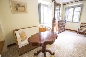 Une pièce comprenant un canapé en osier, une table en bois, une commode et une fenêtre avec des rideaux.