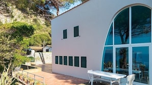 Una casa moderna con fachada blanca, un patio con mesa y sillas, y un ventanal grande.