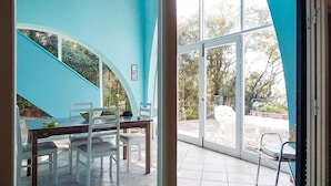 Comedor con mesa y sillas, pared azul y vista a través de grandes ventanales.