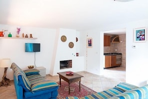 Una sala de estar con un sofá, una mesita de centro y un televisor. Se ve una cocina al fondo.