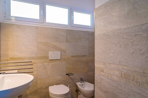 Un baño moderno con un lavamanos grande, inodoro, bidé y una ventana sobre el inodoro.