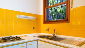 Een keuken met gele tegels, een raam, een spoelbak en een fornuis.