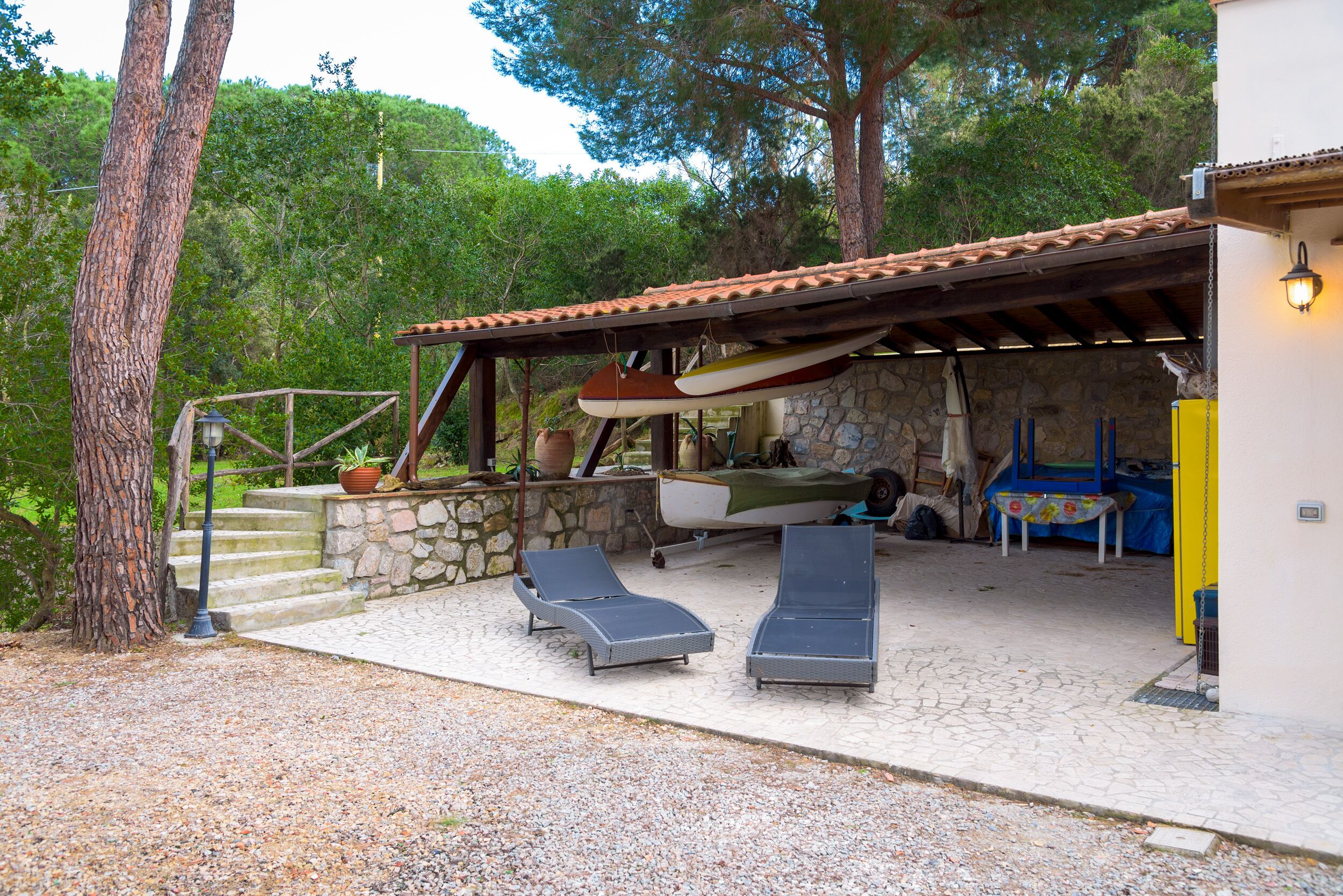 A covered outdoor area with two lounge chairs, a stone wall, and a boat.