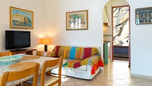 A living room with a TV, a sofa, a table with chairs, and paintings on the walls. - Villino Forno (Portoferraio)