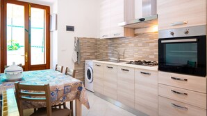 A compact kitchen with a washing machine, a stove, and a dining area with a table and chairs. - Villino La Fontanella (Portoferraio)
