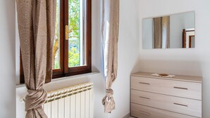 A bedroom with a window, a radiator, a wooden dresser, and a mirror on the wall. - Villino La Fontanella (Portoferraio)