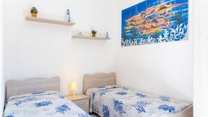 A bedroom with two beds, a nightstand, a lamp, and a painting on the wall. - Villino La Fontanella (Portoferraio)