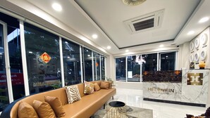 En moderne hotellobby med en lædersofa, en marmorreception og store vinduer med udsigt over byen.