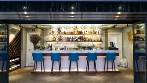 En bar med en bordplade i marmor, tre blå barstole og et vinskab.