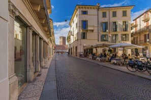 A cobblestone street lined with buildings, outdoor seating at cafes, and a distant castle.