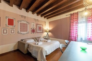 Quarto com cama, mesa de cabeceira, abajur e janela com cortinas.