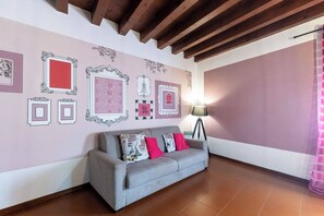 A room with a grey sofa, a floor lamp, and a wall decorated with framed pictures.