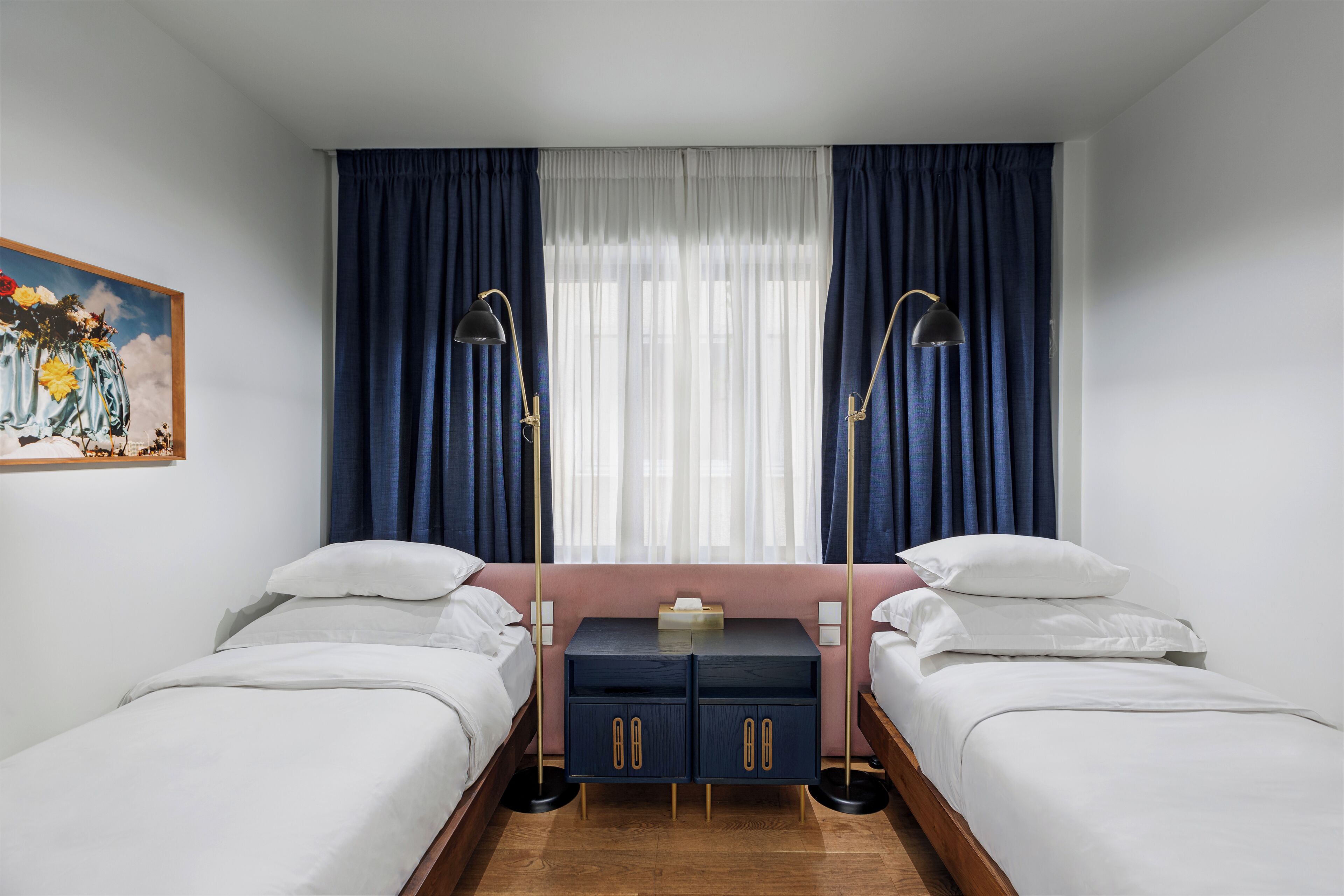 A room with two beds, a nightstand, and a painting on the wall.