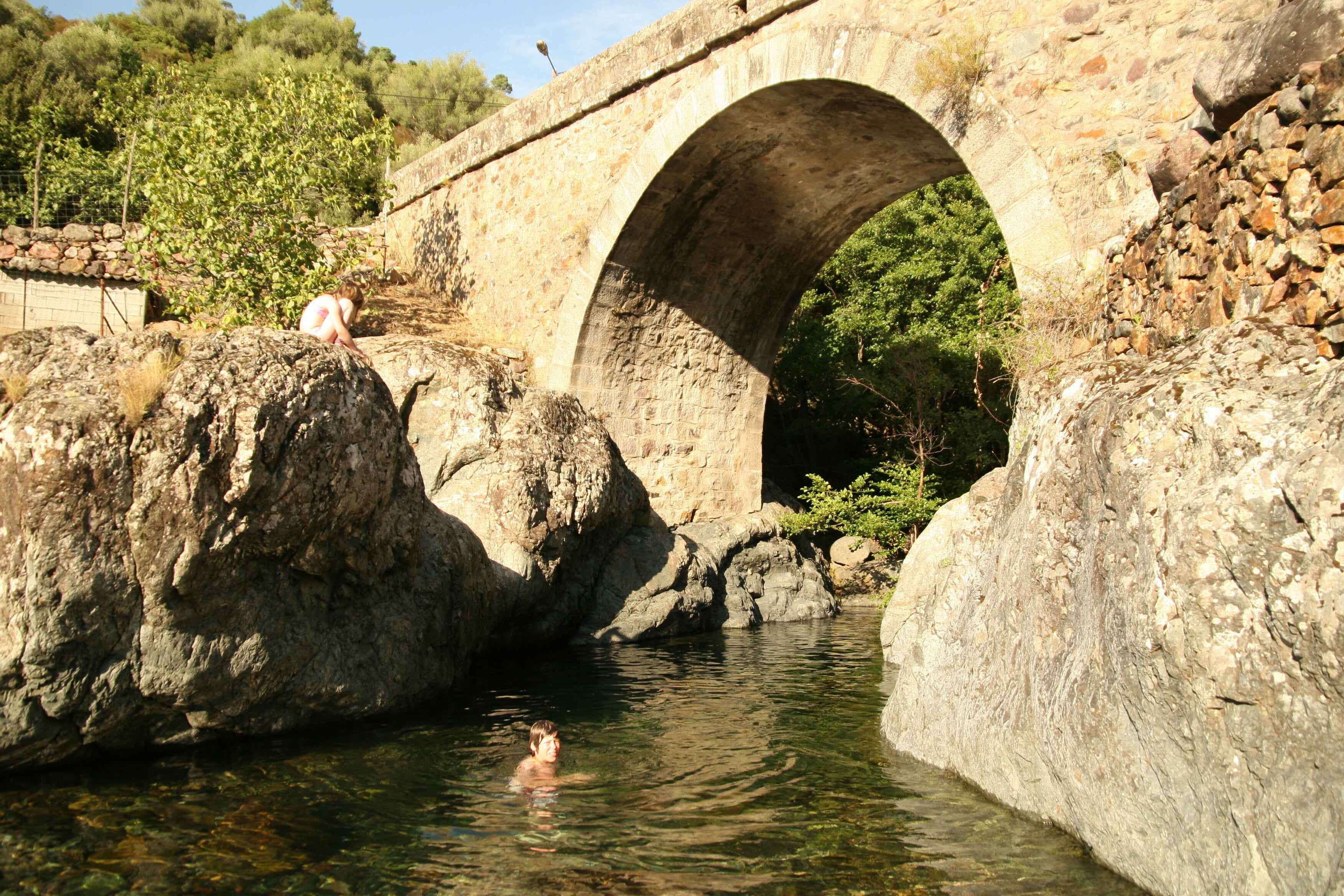 A stone bridge over a clear water body with a person swimming.