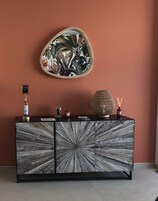 Un mueble de madera con diseño radial, un espejo decorativo y una pequeña mesa con velas y una botella.