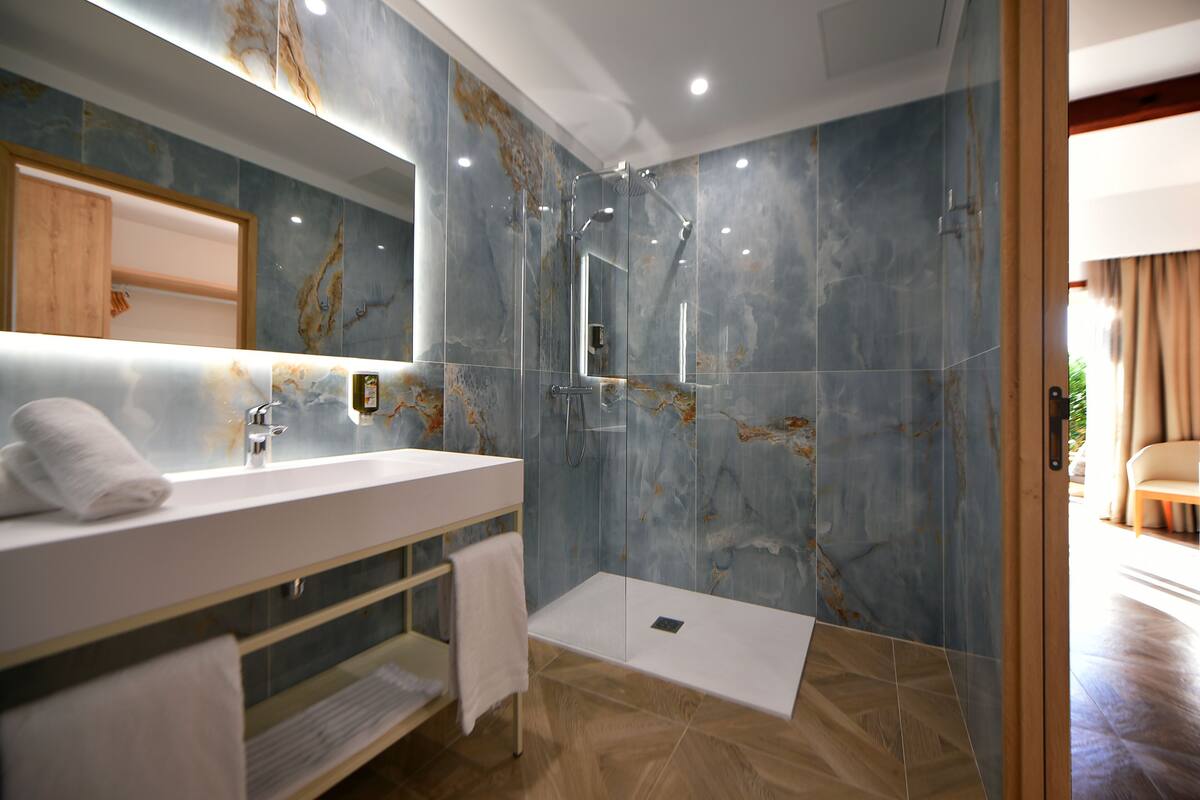 A modern bathroom with a large mirror, a white vanity, and a glass-enclosed shower.