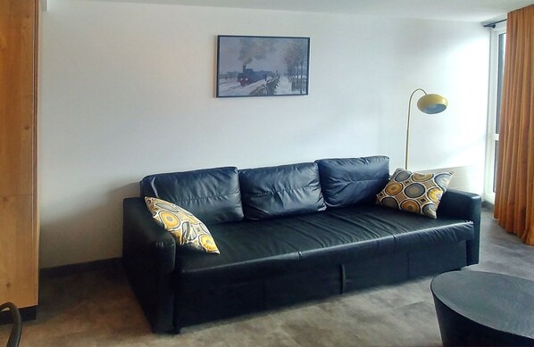 A black leather sofa with patterned cushions, a floor lamp, and a framed painting on the wall.