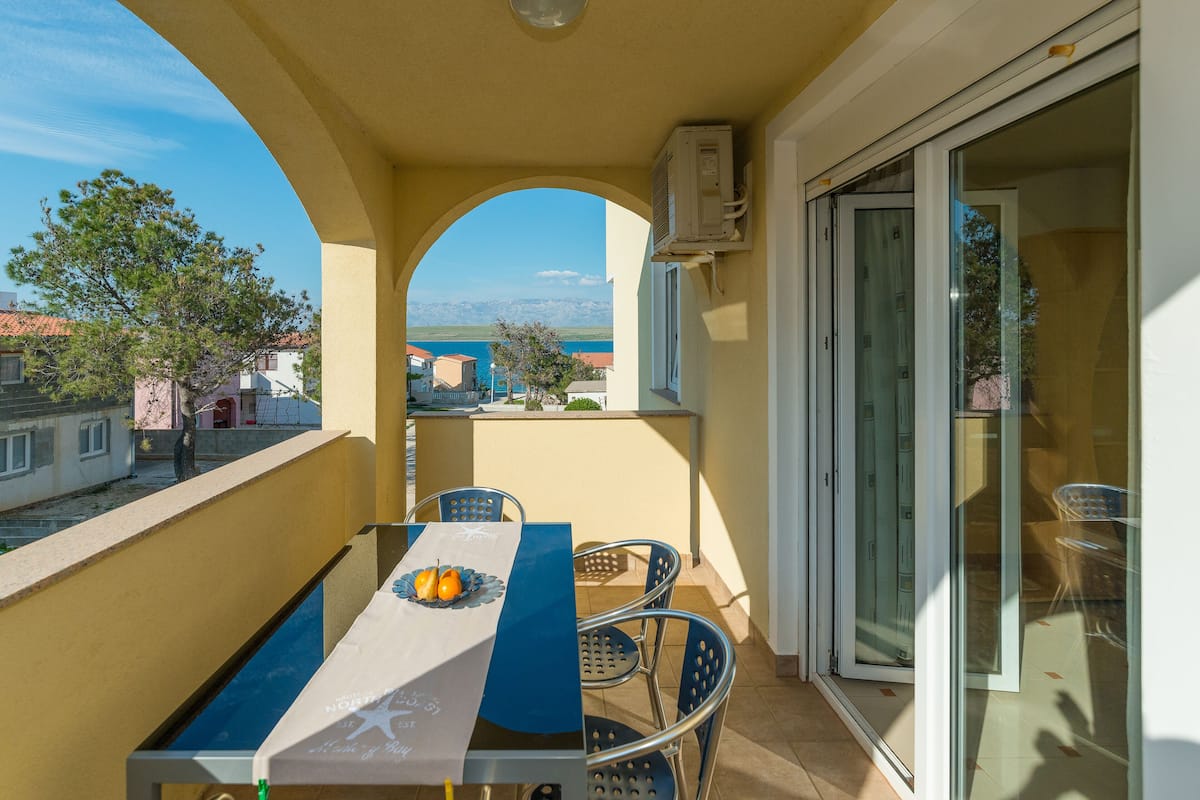 Ein Balkon mit Tisch und Stühlen, Blick auf das Meer und eine Glastür zu einem Außenbereich.
