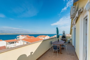 Un balcon avec une table, des chaises et un barbecue, offrant une vue sur la mer.