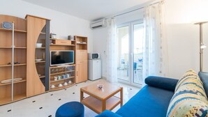 En moderne stue med en blå sofa, træhylder, et fjernsyn og et lille bord.