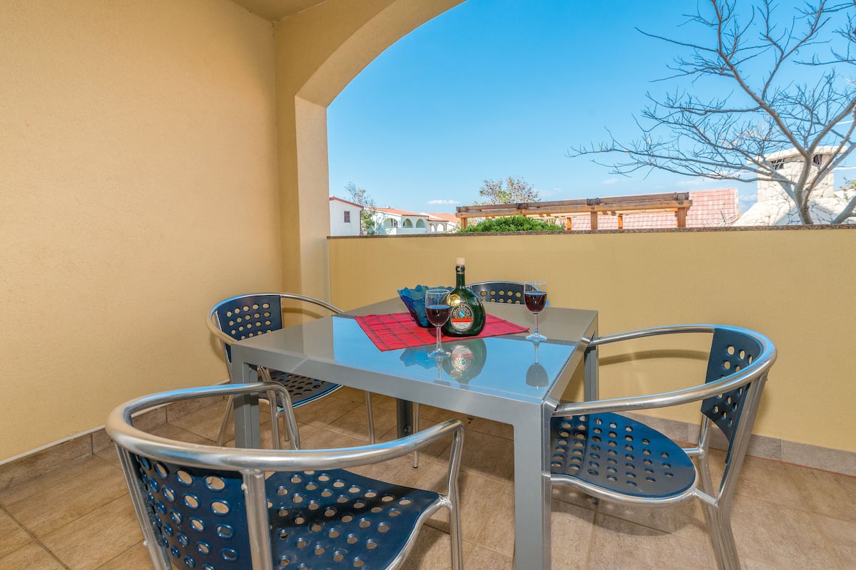 Ein Balkon mit Glastisch, vier Stühlen und einer Weinflasche.